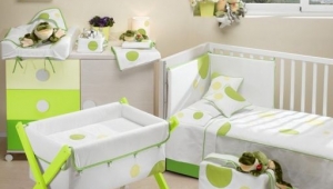 DORMITORIO INFANTIL CON CUNA , CUCO Y CÓMODA CAMBIADOR DE CAJONES Y PUERTA. DIFERENTES TEXTILES PARA VESTIR LOS MUEBLES DE PUERICULTURA.