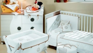 DORMITORIO INFANTIL CON CUNA , CUCO Y CÓMODA CAMBIADOR DE CAJONES Y PUERTA. DIFERENTES TEXTILES PARA VESTIR LOS MUEBLES DE PUERICULTURA.