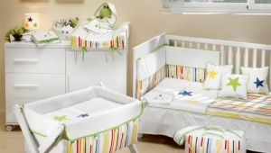 DORMITORIO INFANTIL CON CUNA , CUCO Y CÓMODA CAMBIADOR DE CAJONES Y PUERTA. DIFERENTES TEXTILES PARA VESTIR LOS MUEBLES DE PUERICULTURA.