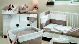 DORMITORIO INFANTIL CON CUNA , CUCO Y CÓMODA CAMBIADOR DE CAJONES Y PUERTA. DIFERENTES TEXTILES PARA VESTIR LOS MUEBLES DE PUERICULTURA.