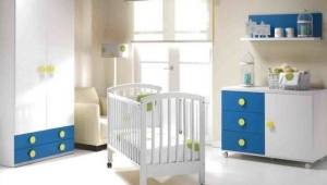 DORMITORIO INFANTIL EN BLANCO Y AZUL, CON ARMARIO DE DOS PUERTAS CON CAJONES VISTOS, CUNA, CÓMODA Y ESTANTE DE PARED. GRAN VARIEDAD DE TEXTILES PARA VESTIR LOS MUEBLES DE PUERICULTURA.