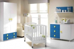 DORMITORIO INFANTIL EN BLANCO Y AZUL, CON ARMARIO DE DOS PUERTAS CON CAJONES VISTOS, CUNA, CÓMODA Y ESTANTE DE PARED. GRAN VARIEDAD DE TEXTILES PARA VESTIR LOS MUEBLES DE PUERICULTURA.